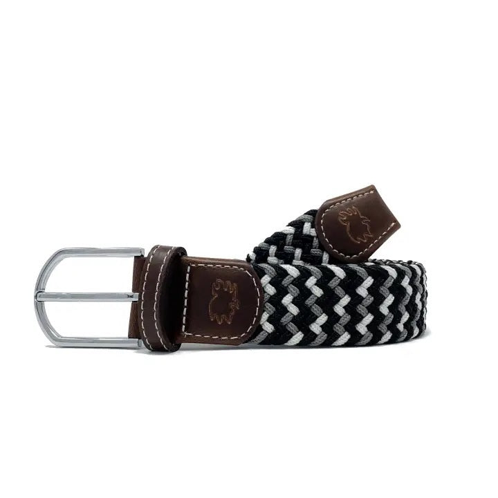 The ROOSTAS BAJA Woven Stretch Belt features a black, white, and gray tri-color weave, silver buckle, brown leather with white stitching, and an embossed ROOSTAS logo.