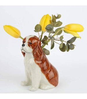 The QUAIL CERAMICS Cavalier King Charles Spaniel Flower Vase by QUAIL DESIGNS, a hand-painted ceramic piece in brown and white, holds yellow tulips and green foliage against a plain white background.