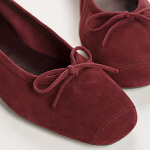 The REQINS - HARMONY Suede Ballerina Flats in Bordeaux, featuring elegant small bows on the toes, are displayed on a plain light background.