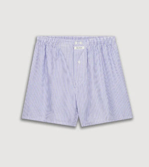 A person models HARTFORD - COTTON BOXER SHORTS in light blue and white stripes with an elastic waistband, standing against a plain beige background.