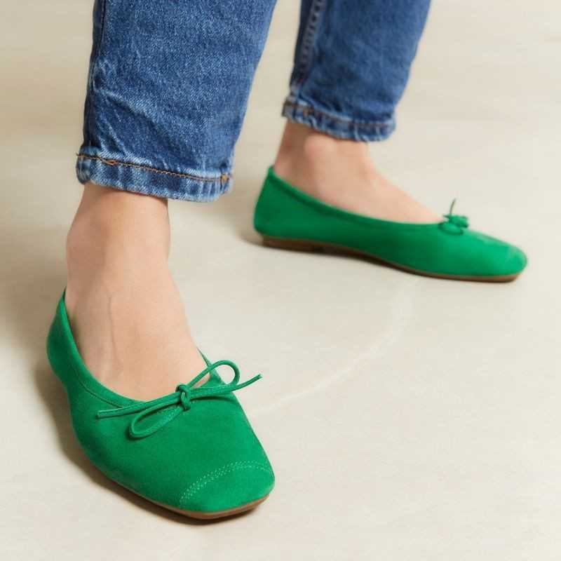 Top view of the REQINS - HARMONY suede ballerina flat in Gazon Green, featuring a small bow on the toe, photographed on a plain light background.