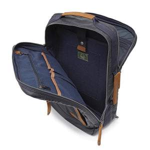 The TSD BRAND - MADRONE COATED CANVAS BACKPACK IN NAVY features brown leather accents, a spacious main compartment, a padded laptop sleeve with snap closure, and multiple zippered pockets on the inside flap.