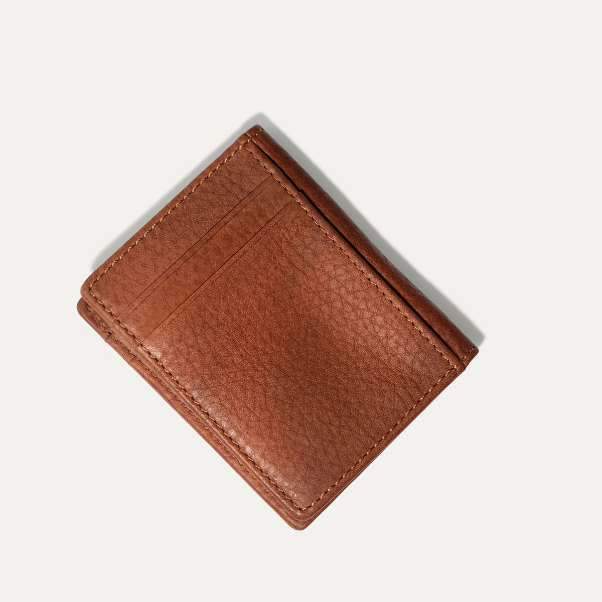 The WILL LEATHER GOODS Classic Money Clip sits atop an open full-grain leather wallet, both in brown, showcasing card slots against a plain light background.