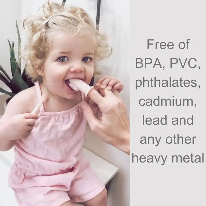 A child with curly blonde hair in a pink outfit is seated, holding a light-colored popsicle with the assistance of an adult's hand. Text on the right side of the image reads: "Free of BPA, PVC, phthalates, cadmium, lead and any other heavy metal," highlighting the importance of safe materials for good oral hygiene using the SILICONE FINGER TOOTHBRUSH AND TONGUE CLEANER by ALI + OLI.