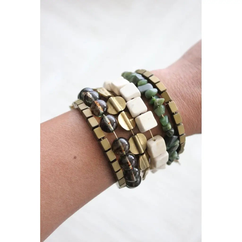 The DAVID AUBREY ATHENA HEMATITE GLASS AGATE JADE WRAP BRACELET, by DAVID AUBREY, features metallic gold square beads, transparent and ivory geometric accents—an elegant Mother&#39;s Day gift displayed on a gray background.