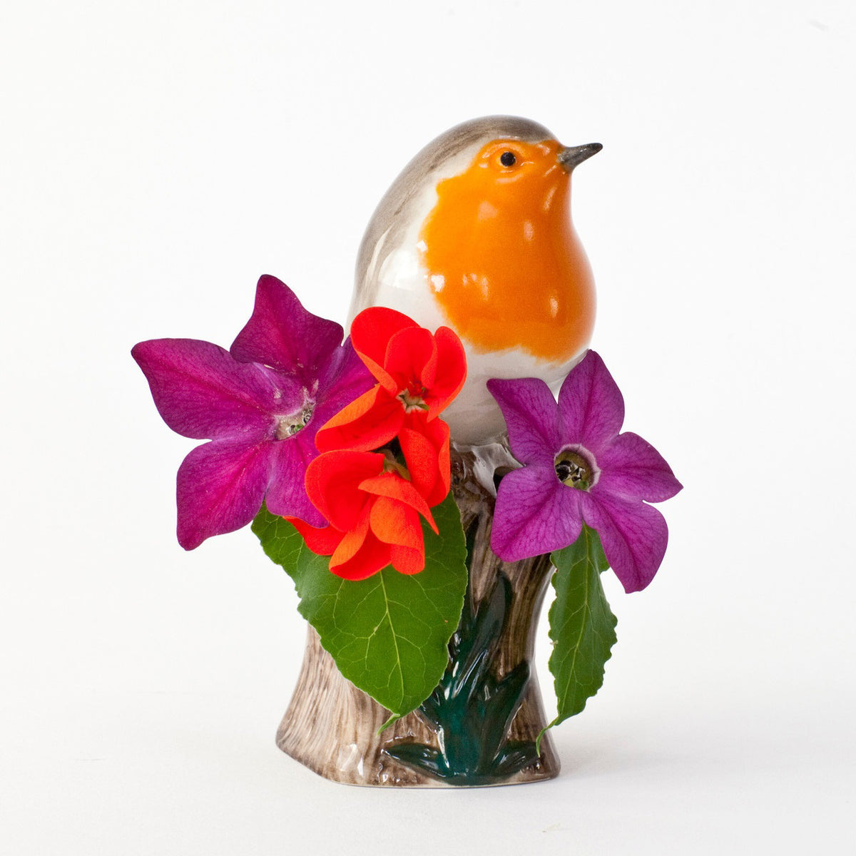 The QUAIL CERAMICS - ROBIN BUD VASE by QUAIL DESIGNS is a handpainted stoneware vase featuring a ceramic robin with an orange breast perched on a leafy tree stump on a white background.