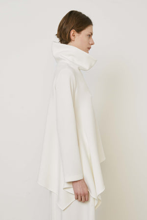 A person with brown hair faces away wearing the MEIMEIJ ASYMMETRICAL COWLNECK TOP in lightweight scuba fabric, featuring an asymmetrical hem, paired with matching white bottoms, against a plain white background.