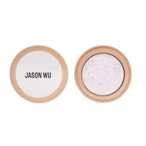 A small circular container of Jason Wu Beauty's "Ready to Shimmer Ethereal 1" eyeshadow. The cream eyeshadow is light-colored with an ethereal shimmer effect. The container features a beige-colored rim with the brand name "JASON WU BEAUTY" written in bold, black letters on the clear top.