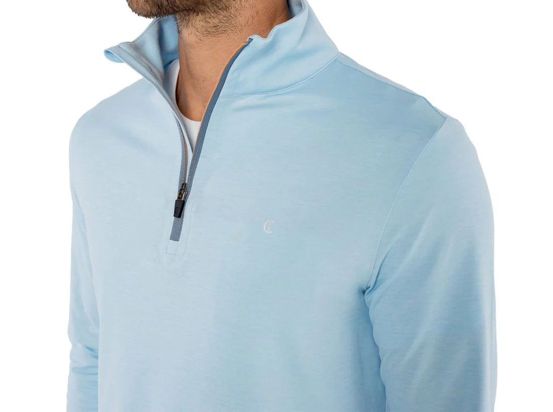 A man wears the CRIQUET Feather Performance Knit Quarter Zip Pullover in Heather Blue, featuring brrr° technology and a small embroidered logo on the chest, over a white T-shirt. His face is partially out of frame.