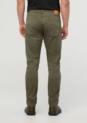 A person stands facing away from the camera against a plain background, wearing DUER - NO SWEAT ATHLETIC TAPER PANTS IN KELP paired with brown shoes.