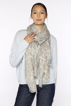 A woman poses against a white background wearing a light pink sweater, blue jeans, black shoes, and the KINROSS CASHMERE - PEBBLE PRINT SCARF by KINROSS in a silk cashmere blend draped over her shoulders.
