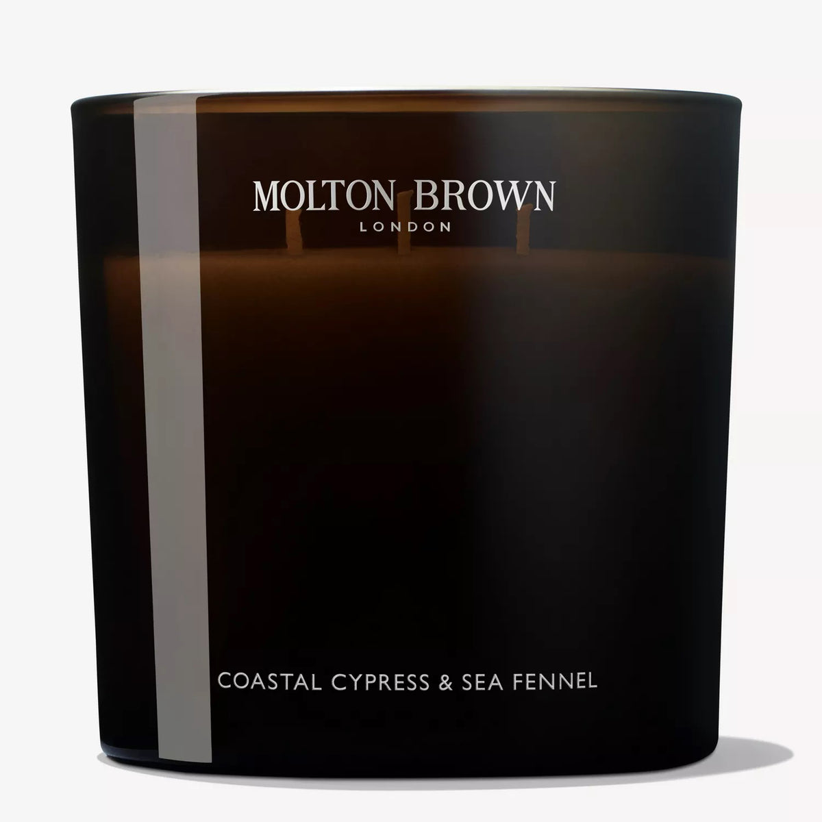 The MOLTON BROWN - COASTAL CYPRESS 3 WICK CANDLE, in dark frosted glass with white branding, features marine notes and the refreshing scent of a sea breeze.