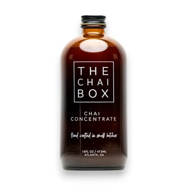 The Chai Box's brown glass bottle, prominently labeled with "THE CHAI BOX - CHAI CONCENTRATE," features text that reads "Hand crafted in small batches" and specifies a volume of 16 fl oz / 473 ml. Made with the finest spices, the label proudly displays "Atlanta, GA" at the bottom. The bottle is topped with a black screw cap.
