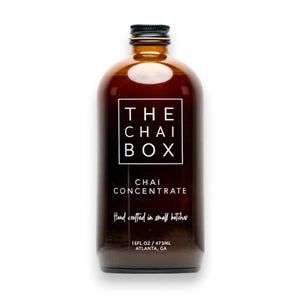 The Chai Box's brown glass bottle, prominently labeled with "THE CHAI BOX - CHAI CONCENTRATE," features text that reads "Hand crafted in small batches" and specifies a volume of 16 fl oz / 473 ml. Made with the finest spices, the label proudly displays "Atlanta, GA" at the bottom. The bottle is topped with a black screw cap.