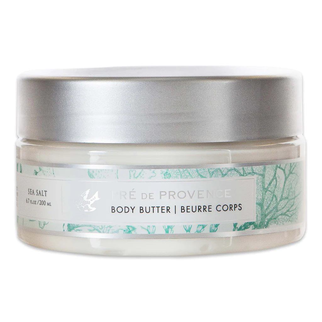 A clear jar with a silver lid contains BODY BUTTER - SEA SALT from EUROPEAN SOAPS, LLC, infused with Shea Butter. The label describes a sea salt scent and details 6.7 fl oz / 200 ml. The design features light green botanical illustrations on a white background, promising luxurious moisturization for your skin.