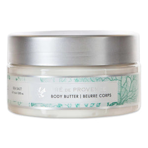 A clear jar with a silver lid contains BODY BUTTER - SEA SALT from EUROPEAN SOAPS, LLC, infused with Shea Butter. The label describes a sea salt scent and details 6.7 fl oz / 200 ml. The design features light green botanical illustrations on a white background, promising luxurious moisturization for your skin.