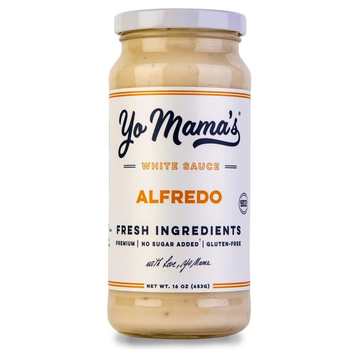 Two plates with large slices of chicken Alfredo pizza, made with fresh cream and parmesan cheese, sit beside a jar of YO MAMA'S - CLASSIC ALFREDO by YO MAMA'S FOODS, a bowl of red pepper flakes, a pizza tray, and a green napkin on a white surface.