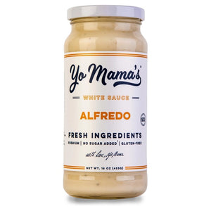 Two plates with large slices of chicken Alfredo pizza, made with fresh cream and parmesan cheese, sit beside a jar of YO MAMA'S - CLASSIC ALFREDO by YO MAMA'S FOODS, a bowl of red pepper flakes, a pizza tray, and a green napkin on a white surface.