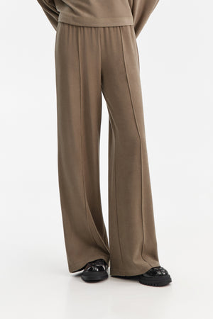 The ELEH - THE SCALA PULL ON SWEATPANT TROUSER by ELEH is a pair of loose-fitting, light brown, velvety pull-on trousers with an elastic waistband, shown against a plain white background.