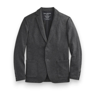 A man fastens the MACK WELDON Ace Blazer in Charcoal Heather over a gray hoodie, white tee, and dark jeans, paired with white sneakers with beige soles. He stands against a plain background, looking slightly to the side.