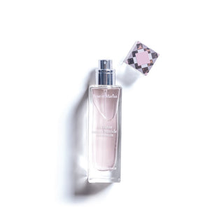 A rectangular glass perfume bottle with a silver spray nozzle and square cap beside it casts a shadow on white. The label reads "ROSE ET MARIUS - A SIESTA IN A SUNLIT HOME EAU DE PARFUM 30ML," evoking the scent of Provence.