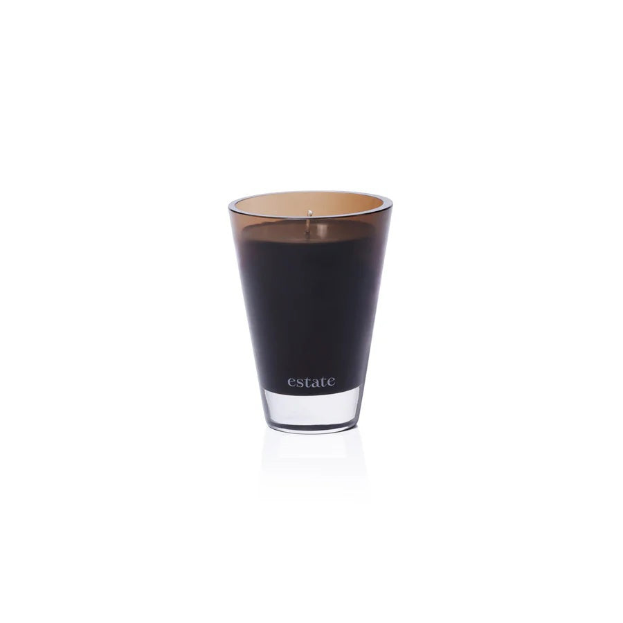 The ZODAX Thistle Estate Candle (10.5 oz) in black is displayed in a glass holder beside its matching box, both reflecting the fresh California coast fragrance.