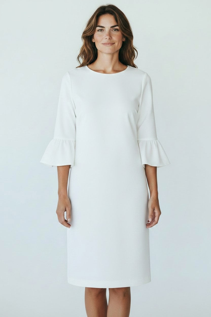 A woman with wavy brown hair smiles softly, facing forward in a knee-length 0039 ITALY - MAXLIN DRESS featuring three-quarter trumpet sleeves and ruffled cuffs. The white dress by 0039 ITALY looks comfortable against a plain light background.