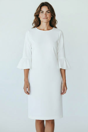 A woman with wavy brown hair smiles softly, facing forward in a knee-length 0039 ITALY - MAXLIN DRESS featuring three-quarter trumpet sleeves and ruffled cuffs. The white dress by 0039 ITALY looks comfortable against a plain light background.