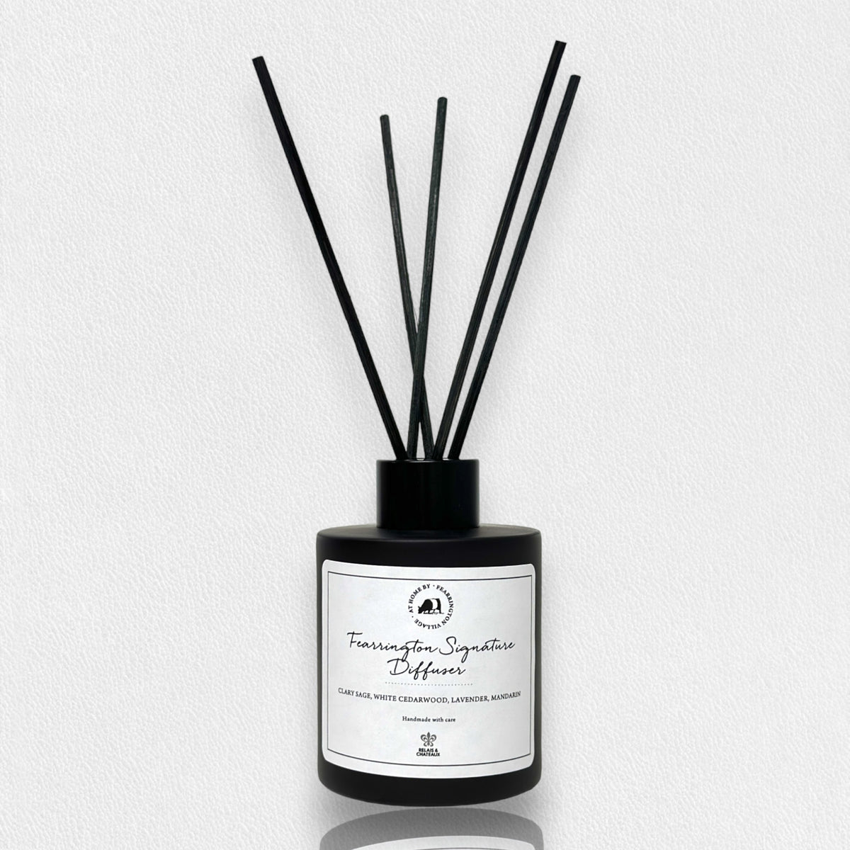 Housed in a sleek black bottle with five slender black reeds, the FEARRINGTON SIGNATURE DIFFUSER from the FEARRINGTON SIGNATURE COLLECTION by FEARRINGTON VILLAGE - HOME DECOR features a white label displaying "Fragrance Signature Diffuser" and scent notes of cedarwood, lavender, and amber. Inspired by the tranquil allure of Fearrington Village, this sophisticated reed diffuser is ideal for anyone who appreciates the calming atmosphere created by a lavender candle.