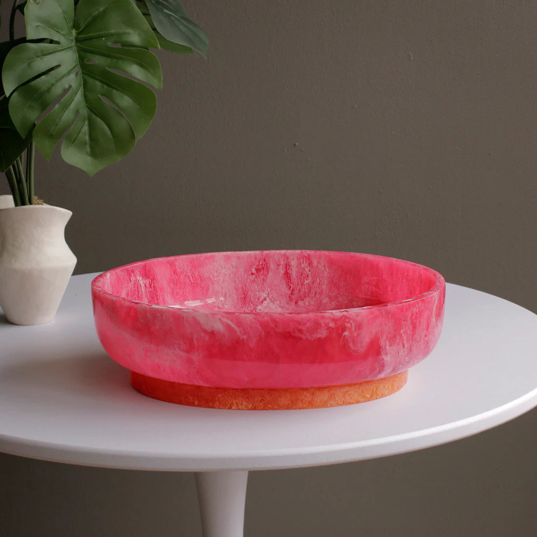 The BEATRIZ BALL RIO Oval Bowl with Base features a glossy, pink marbled finish and a contrasting tan base, displayed against a white background.