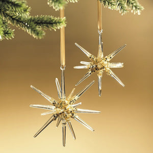 Two 4.75-inch GLASS 3D SNOWFLAKE ORNAMENT SMALL star-shaped glass ornaments with gold glitter accents hanging from a pine branch.