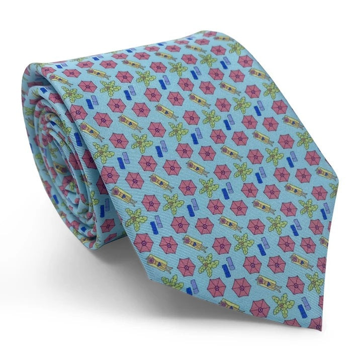 The BIRD DOG BAY PETER-BLAIR - SUNSCREEN SILK TIE IN AQUA showcases a lively print of pink beach umbrellas, green palm trees, and blue rectangles on an aqua silk background. Rolled neatly on a white surface, this playful accessory is handmade in New York and finished with the iconic Peter-Blair woven label.
