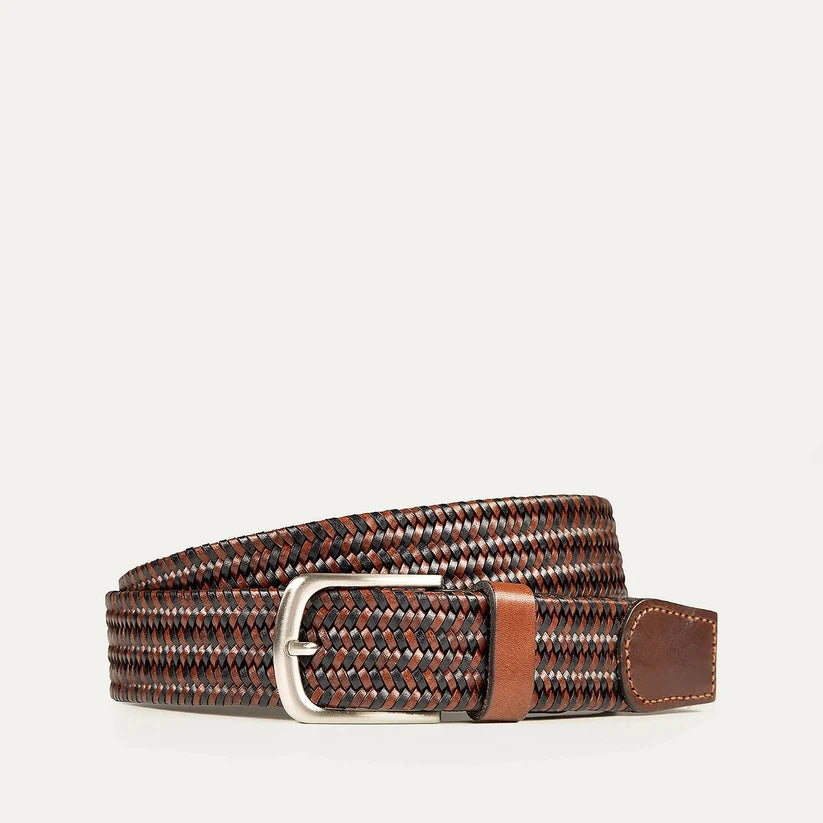 The WILL LEATHER GOODS - STRETCH BELT features a green, purple, and black braided design with full-grain leather accents by the silver buckle and tip, shown on a plain light background. Brand: WILL LEATHER GOODS.