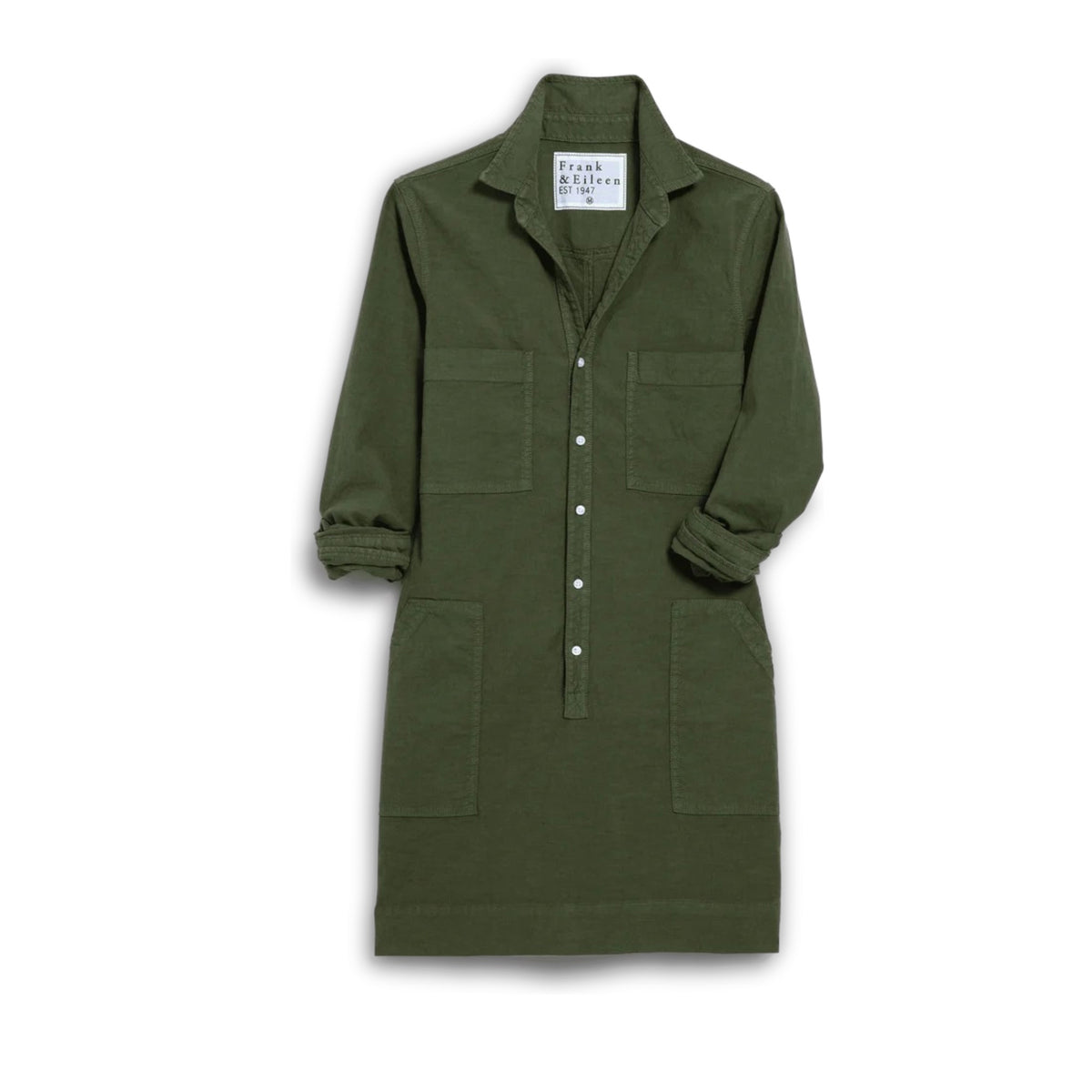 A woman with long brown hair smiles indoors, wearing the FRANK &amp; EILEEN SOUTHERN IRELAND UTILITY DRESS in Hunter Green. She stands by a beige armchair and lamp, with patterned wallpaper in the background.