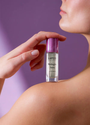 A clear glass bottle labeled “LAFCO - FINE FRAGRANCE, MIDNIGHT AURA 10ML” with a shiny pink cap rests against a white background, highlighting this elegant vegan fragrance from LAFCO in a convenient travel-size option.