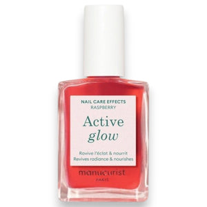 A pink serum drop labeled with its ingredients: raspberry extract (strengthens nails), AHAs (restore and harden), and sweet almond oil (nourishes). The text highlights that MANUCURIST - ACTIVE GLOW CARE POLISH by MANUCURIST INC is 85.5% plant-based—making it the ideal nail strengthener for achieving healthy, glass-like nails.