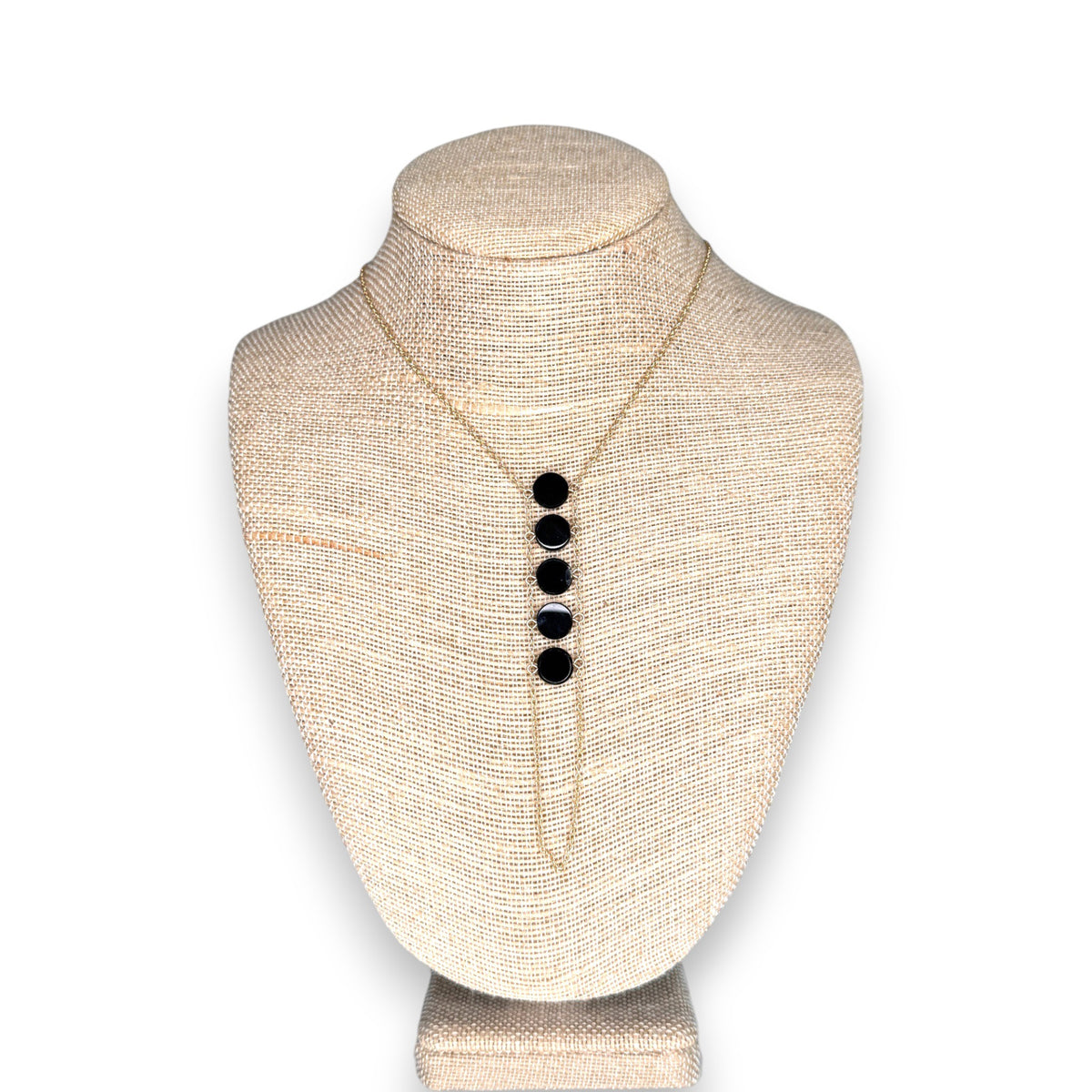 The GOLDISH - Ladders to Bliss Black Onyx Circle Stone Necklace by GOLDISH is shown on a beige fabric bust, with five round black onyx pendants in a vertical row symbolizing balance and harmony.