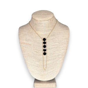 The GOLDISH - Ladders to Bliss Black Onyx Circle Stone Necklace by GOLDISH is shown on a beige fabric bust, with five round black onyx pendants in a vertical row symbolizing balance and harmony.