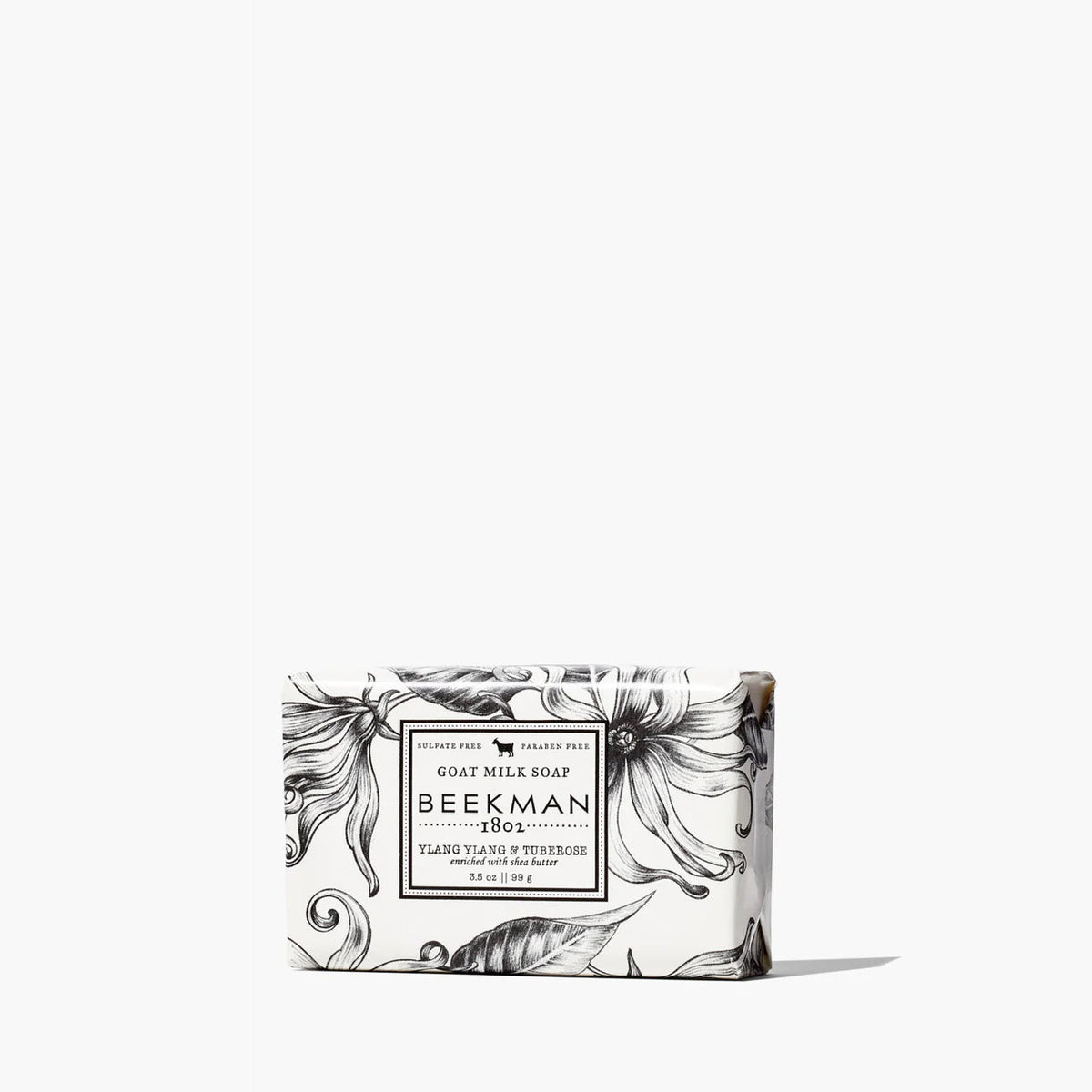 A rectangular 3.5oz BEEKMAN - YLANG YLANG AND TUBEROSE BAR SOAP by BEEKMAN - STA ELEMENTS sits on a white background, wrapped in white paper with black floral designs and a label highlighting its goat milk formula.