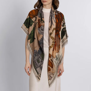 The SABINA SAVAGE ENGLAND Oranges and Lemons Cashmere Scarf in Citrine/Zest showcases intricate illustrations of an orange slice, exotic citrus fruits, vibrant green feathers, a dragon, architectural details in muted tones, and the partially visible word "ELEMENTS" at the bottom.