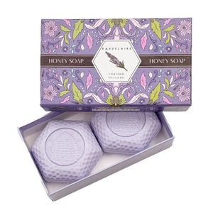 The BAUDELAIRE - LAVENDER HONEY SOAP 3.5 OZ, 2 BAR GIFT BOX features two hexagonal, triple-milled soaps with a beehive design, nestled in a decorative purple floral box and partially opened to reveal the lavender-colored bars inside.
