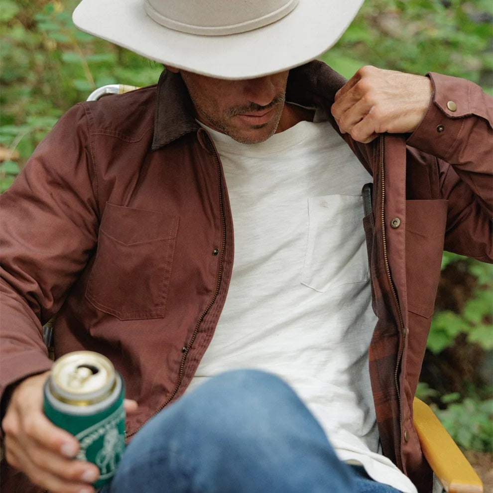 Close-up of the interior of a brown plaid CRIQUET - WAXED RANCH JACKET IN BOURBON, showing a white “Clubhouse Collection” brand label with a blank line for a player’s name.