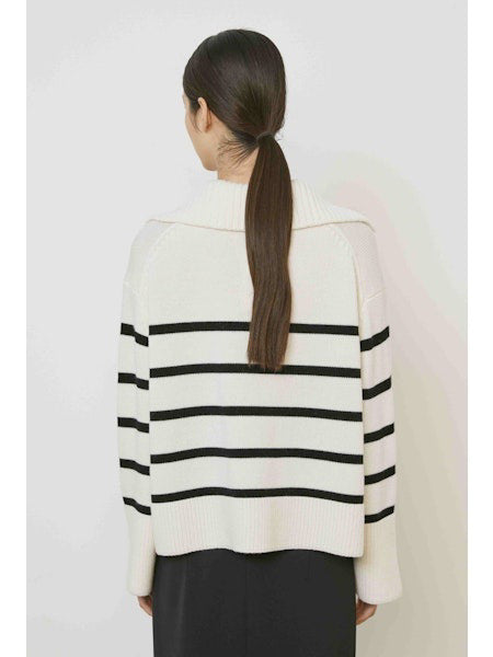 A woman with straight dark hair models the MEIMEIJ STRIPE SWEATER—a cream sweater with black horizontal stripes and a large collar—paired with a plain black skirt, standing against a white background.
