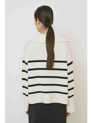 A woman with straight dark hair models the MEIMEIJ STRIPE SWEATER—a cream sweater with black horizontal stripes and a large collar—paired with a plain black skirt, standing against a white background.