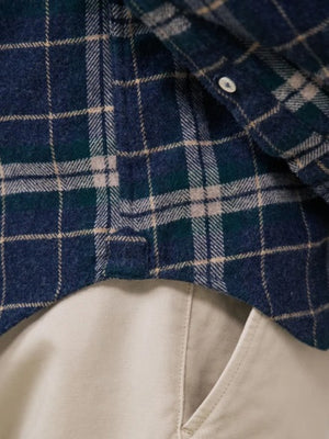 A young person with dark hair, wearing the HARTFORD - PITT CHECKED FLANNEL SHIRT IN BLUE AND GREEN by HARTFORD, looks at the camera while adjusting the shirt collar with one hand against a plain light background.