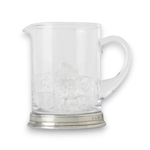 A table set with a martini glass holding an olive, a MATCH - BRANCH BAR PITCHER with a long spoon, a bottle of vodka, a bowl of nuts, a cheese plate, and red roses in the background.