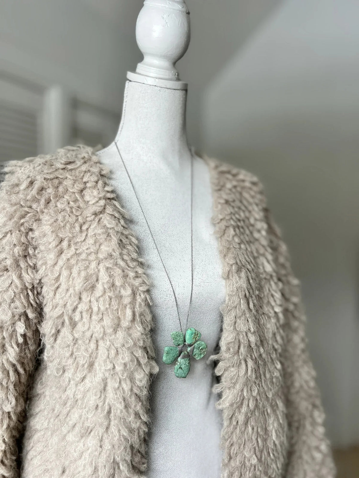 The ANN LIGHTFOOT - ROUGH CUT CHRYSOPRASE FLOWER NECKLACE by ANN LIGHTFOOT features four irregular green chrysoprase stones arranged in a flower-like shape, secured with wrapped cord and suspended from a delicate silver chain, shown against a white background.