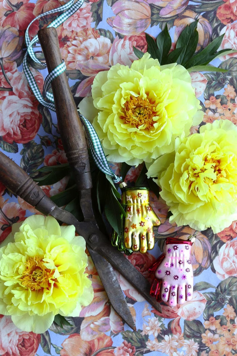 Two GARDENING GLOVES ORNAMENT glass decorations, one pink with purple flowers and one yellow with orange flowers, hanging from gold strings.