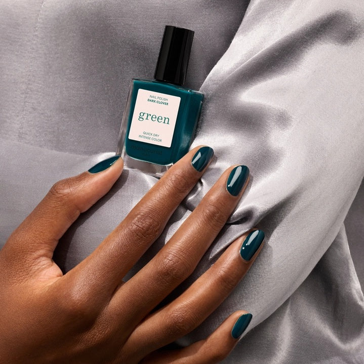A bottle of MANUCURIST - GREEN™ Nail Polish in Dark Clover by MANUCURIST INC showcases a rich dark green hue, complete with a black cap and a beige label stating “green quick dry intense color.” This non-toxic nail polish delivers an intense, vibrant finish while being gentle on your nails.