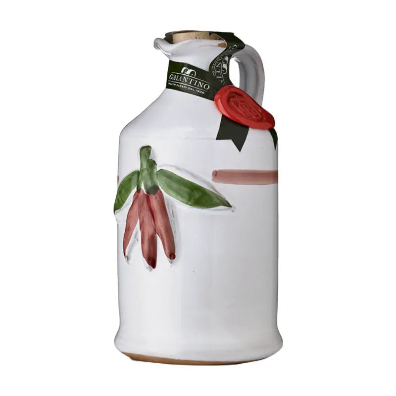 The GALANTINO - PEPERONCINO EXTRA VIRGIN OLIVE OIL by ZIA PIA IMPORTS is presented in a white ceramic jug with a handle, featuring a hand-painted design of red chili peppers and green leaves. The jug is sealed at the neck with a green label and adorned with a red wax seal.